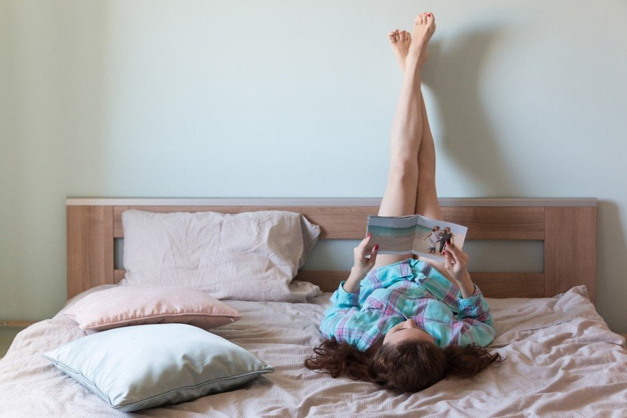 woman doing legs up the wall pose while reading in bed